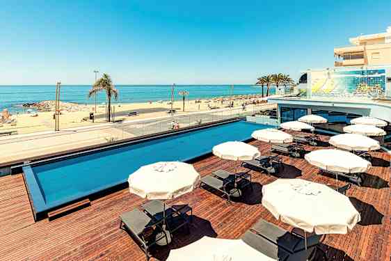 En utomhuspool med solstolar och parasoller, och en sandstrand med havsutsikt. (AI-genererad text)