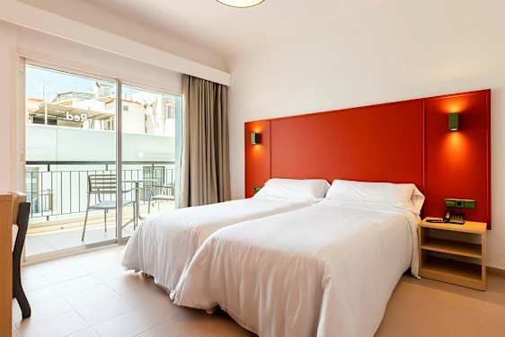 Ett rum med två enkelsängar med vita sängkläder, en röd huvudgavel och en balkong utanför. (AI-genererad text)