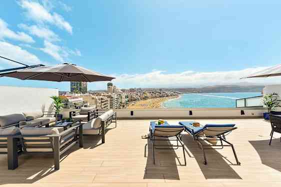 Tak terrass med möbler, parasoll och utsikt över en strand och hav. (AI-genererad text)