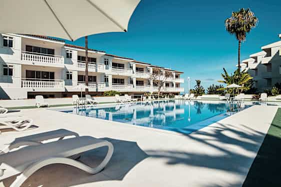 En pool vid ett hotell med solstolar och parasoller. (AI-genererad text)