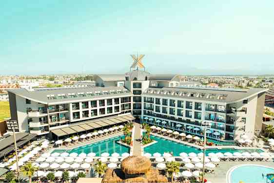 Ett hotellkomplex med en pool och solstolar utomhus, omgiven av grönska och en stad i bakgrunden. (AI-genererad text)