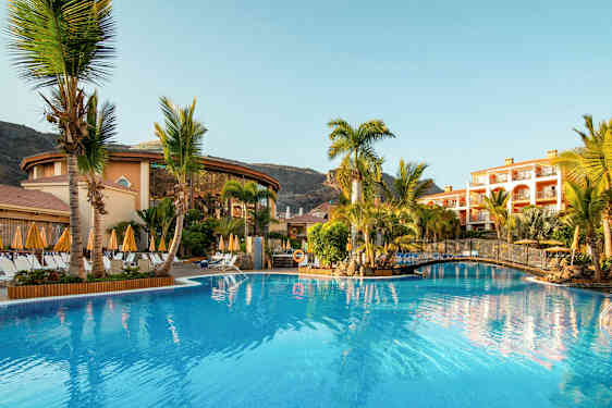 Bild av ett hotellområde med en pool, omgiven av palmer och byggnader. (AI-genererad text)