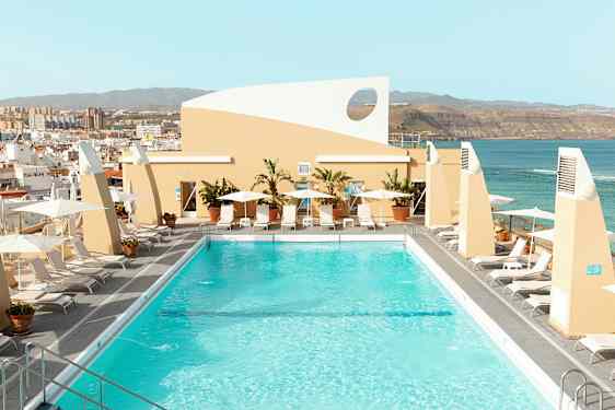 En takpool omgiven av solstolar och parasoller med utsikt över staden och havet. (AI-genererad text)