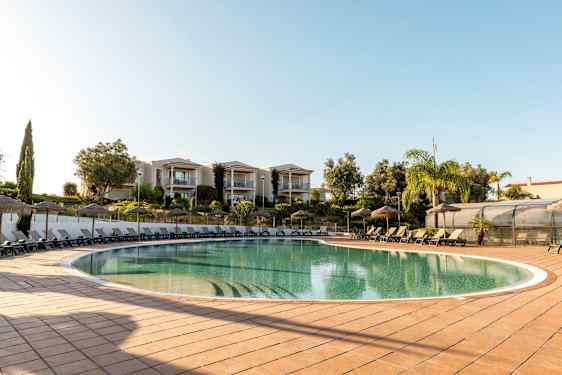 Utomhuspool med solstolar och parasoller, omgiven av grönska och byggnader. (AI-genererad text)