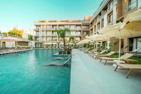 En hotellpool med solsängar och parasoller bredvid moderna byggnader. (AI-genererad text)