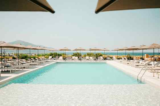 En utomhuspool omgiven av solstolar och parasoller, med utsikt över landskap och hav. (AI-genererad text)