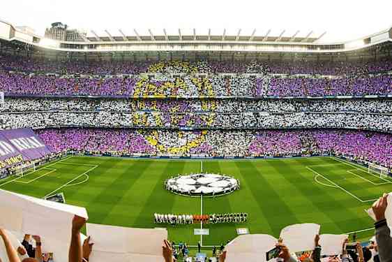 Ett fullt fotbollsstadium med färgat publikmönster och lag på planen. (AI-genererad text)