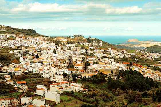 Vy över en stad med många vita byggnader som ligger i en grönskande dal nära havet. (AI-genererad text)