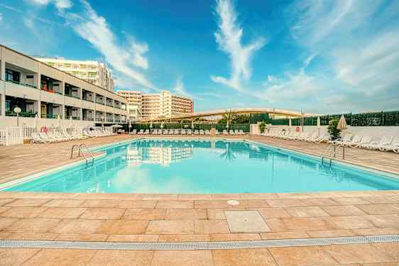 Utomhuspool vid hotell med solstolar och blå himmel. (AI-genererad text)