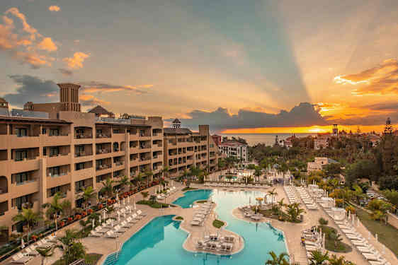 Vy över ett hotell med poolområde vid solnedgången. (AI-genererad text)