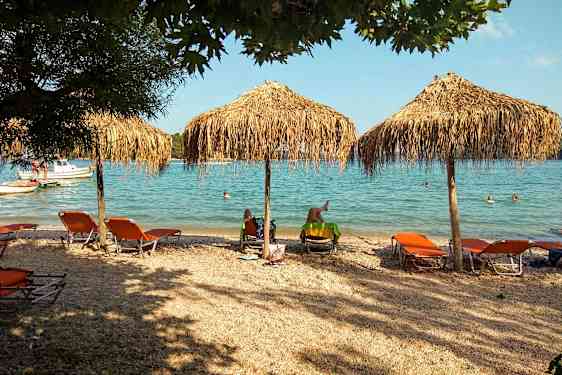 Strand med solstolar och parasoller nära havet, människor simmar i vattnet. (AI-genererad text)
