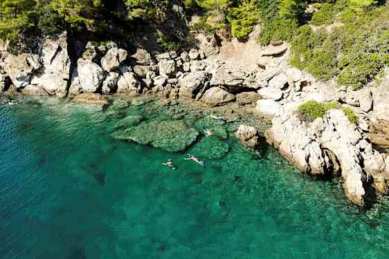 Klart turkost vatten vid en klippig kust, där personer snorklar nära ytan. (AI-genererad text)