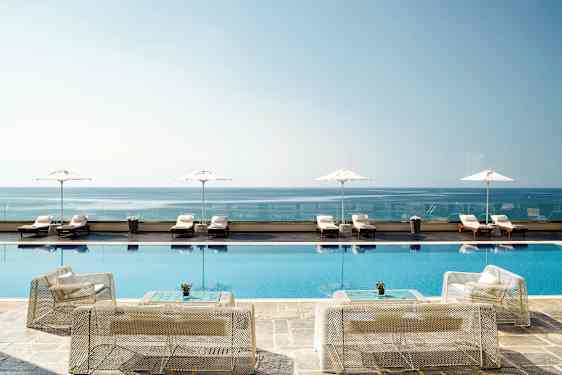 Bild av en infinitypool vid kusten, med solstolar och parasoller i bakgrunden. (AI-genererad text)