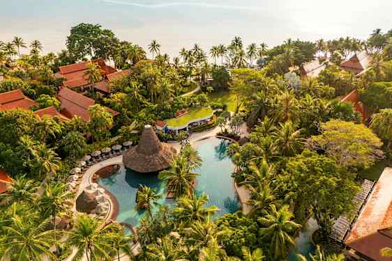 Flygfoto av en tropisk resort med poolområde, grönskande vegetation och traditionellt byggda bungalower. (AI-genererad text)