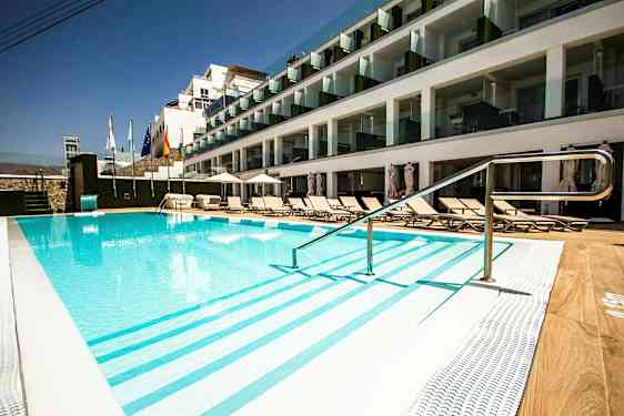 Utomhuspool vid hotell med solstolar och glasbalkonger. (AI-genererad text)