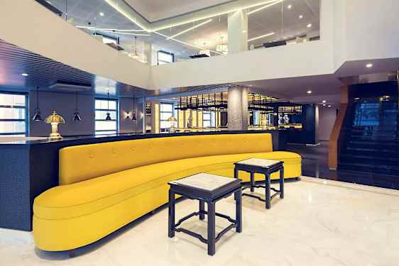 Ett stilfullt inrett utrymme med en gul soffa, små bord och modern belysning. (AI-genererad text)