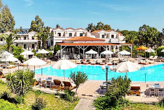 En utomhuspool med solstolar och parasoller, omgiven av grönska och byggnader i bakgrunden. (AI-genererad text)