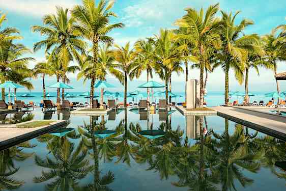 Utomhuspool med palmer och solstolar vid stranden. (AI-genererad text)