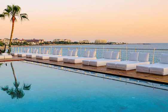 Solstolar vid en pool med utsikt över havet och byggnader i bakgrunden. (AI-genererad text)