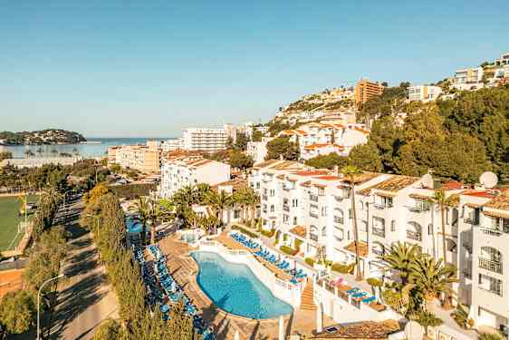 Bild av hotellområde med pool och solstolar, omgivningar med träd och byggnader samt en vy mot havet. (AI-genererad text)