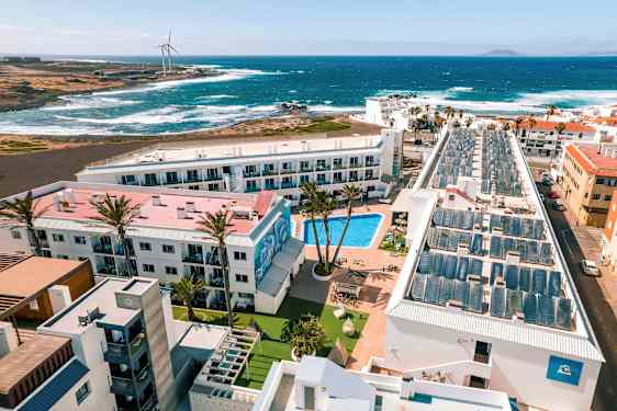 En hotellresort med pool, omgiven av byggnader, med utsikt mot havet och vågarna. (AI-genererad text)