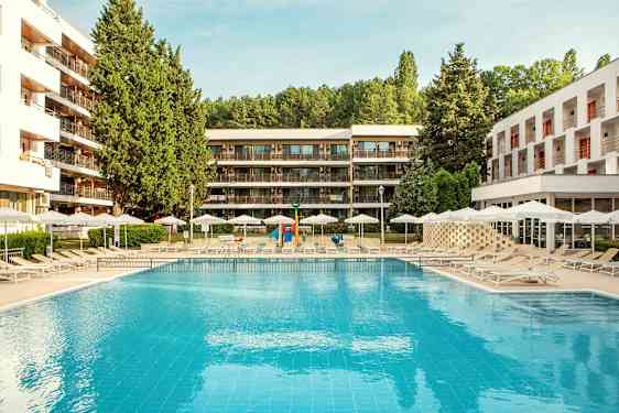 Utomhuspool med solstolar och parasoller, omgiven av moderna byggnader och grönska. (AI-genererad text)