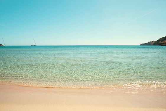 Strand med klart vatten och två segelbåtar i havet. (AI-genererad text)