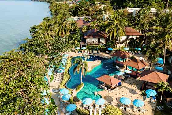 En resort med pool, palmer och parasoller vid havet. (AI-genererad text)