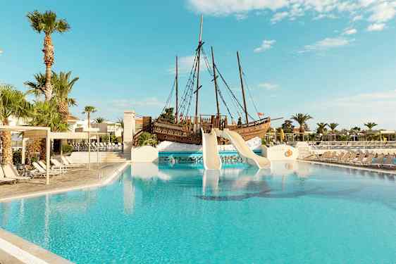 Utomhuspool med rutschkanor från ett piratskepp och omgivande solstolar. (AI-genererad text)