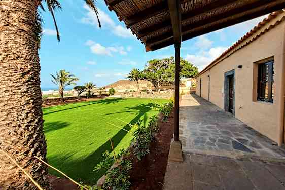 Bild av en byggnad med stenbelagd gång och en trädgård med gräsmatta och palmer. (AI-genererad text)