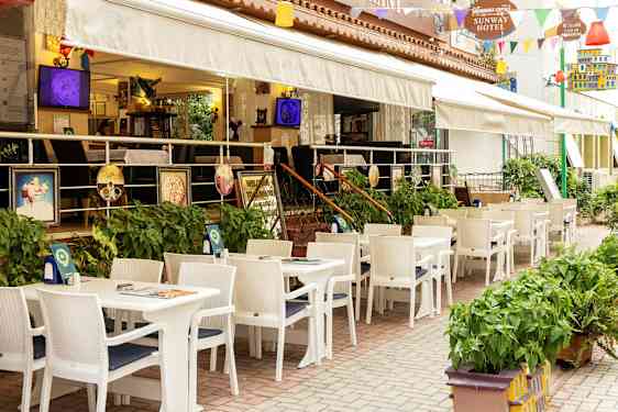 Restaurang med uteservering med vita bord och stolar vid ett hotell. (AI-genererad text)