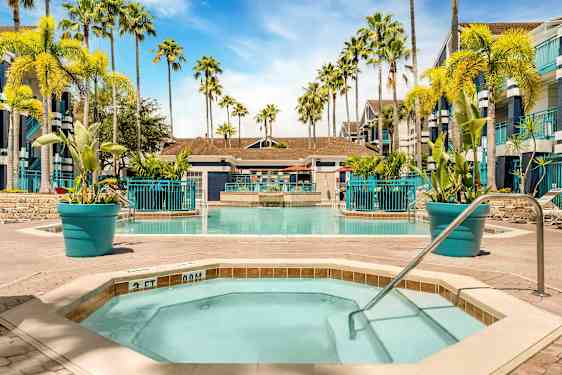 Bild av en pool med omgivande solstolar och palmer. I förgrunden ett mindre bubbelbad med poolräcke. (AI-genererad text)