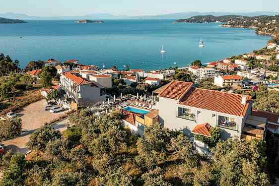 En vy över en kuststad med röda tak på vita byggnader, omgiven av grönska och med blått hav i bakgrunden. (AI-genererad text)