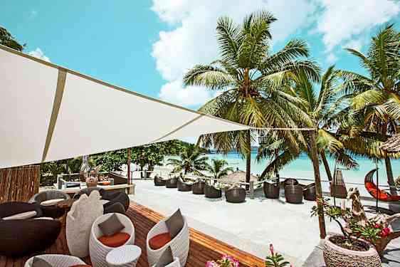 Uteplats med sittplatser och palmträd bredvid en strand. (AI-genererad text)