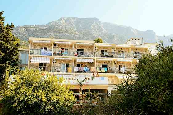 En byggnad med balkonger och hängande handdukar, omgiven av grönska och med berg i bakgrunden. (AI-genererad text)