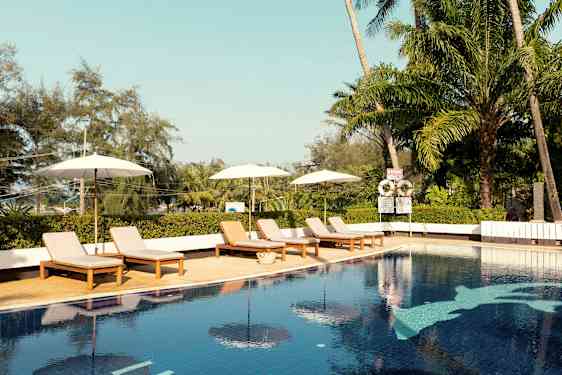 En utomhuspool med solsängar och parasoller. Tropiska träd i bakgrunden. (AI-genererad text)