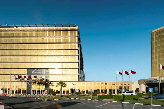 En modern byggnad med guldfärgade glasväggar, omgiven av flaggstänger och en parkeringsplats. (AI-genererad text)