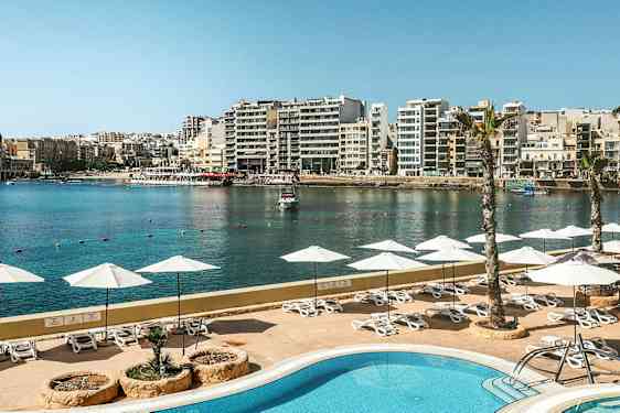 En utsikt över en pool med parasoller och solstolar, med en hamn och stad i bakgrunden. (AI-genererad text)