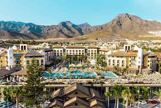 Hotellbyggnader med poolområde och berg i bakgrunden. (AI-genererad text)