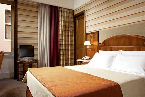 Ett hotellrum med en dubbelsäng, ett skrivbord med en TV och ett fönster. (AI-genererad text)