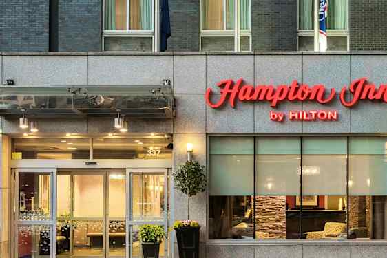 Hotellingång med skylt "Hampton Inn by Hilton" ovanför dörrarna. (AI-genererad text)