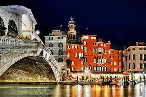 En nattvy av Rialtobron och intilliggande byggnader vid Grand Canal i Venedig. (AI-genererad text)