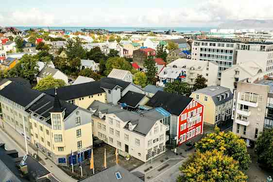 En stadsbild med färgglada byggnader, träd och en väg, samt bakgrund med hav och berg. (AI-genererad text)