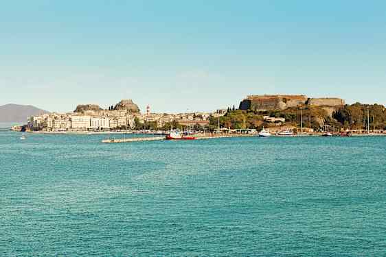 En stad vid havet med historiska byggnader och en fästning på en höjd. (AI-genererad text)