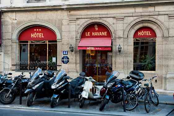 Bild som visar entrén till ett hotell med namnet Le Havane, tre stjärnor visas på markisen. Framför byggnaden står mopeder och cyklar parkerade. (AI-genererad text)