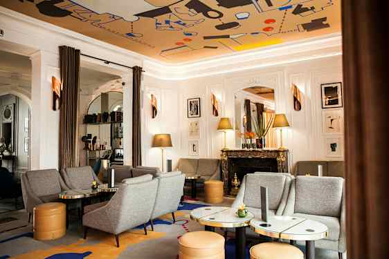 Ett elegant vardagsrum med grå soffor och fåtöljer, marmorbord, en dekorativ eldstad och konstverk på väggen. (AI-genererad text)