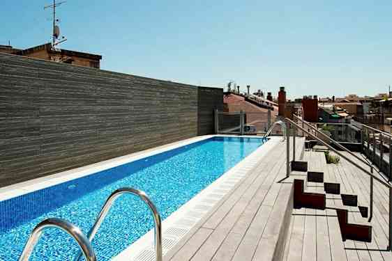 En takterrass med en lång pool omgiven av trädäck och några sittplatser på sidan. (AI-genererad text)