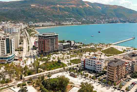 Utsikt över en kuststad med byggnader, grönområden och en pir vid havet. (AI-genererad text)