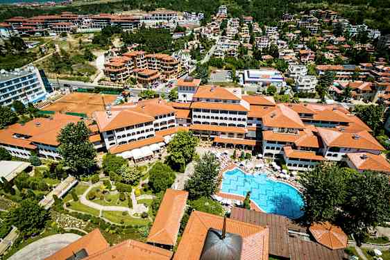 Flygfoto av en semesterort med röda hustak, en pool och omgivande grönområden. (AI-genererad text)