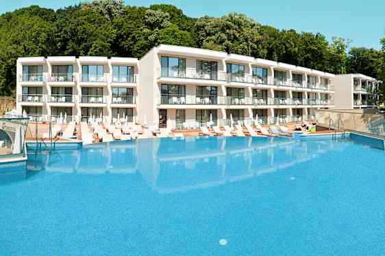 Hotellkomplex med en stor pool framför och solstolar runt omkring. (AI-genererad text)